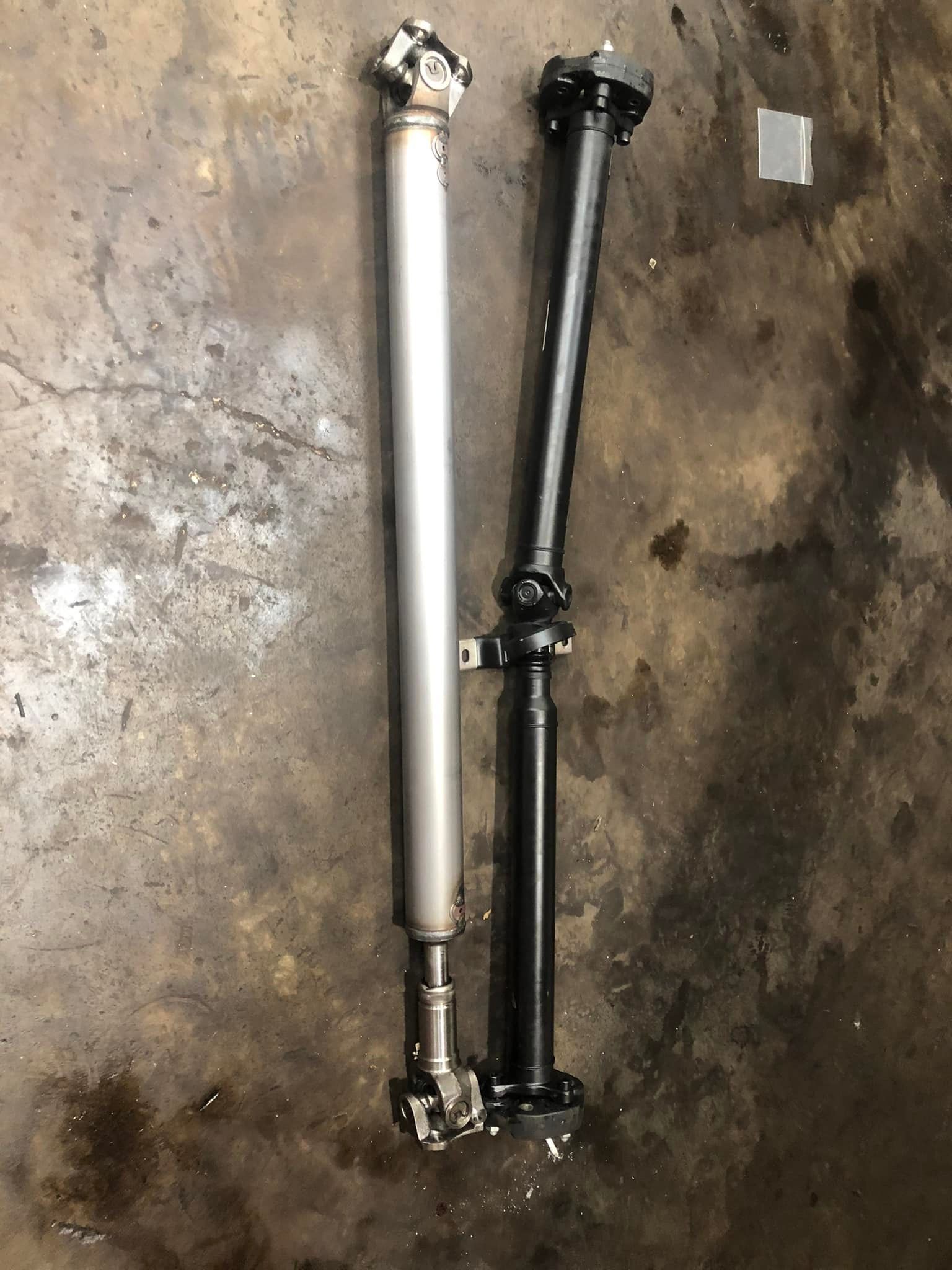 Two drive shafts are sitting next to each other on a concrete surface.