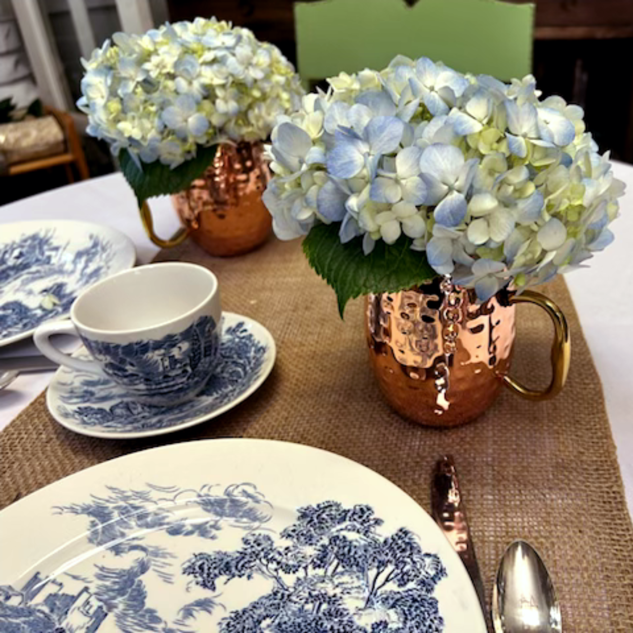 Table setting: copper mugs with blue hydrangeas, blue and white china, burlap runner.