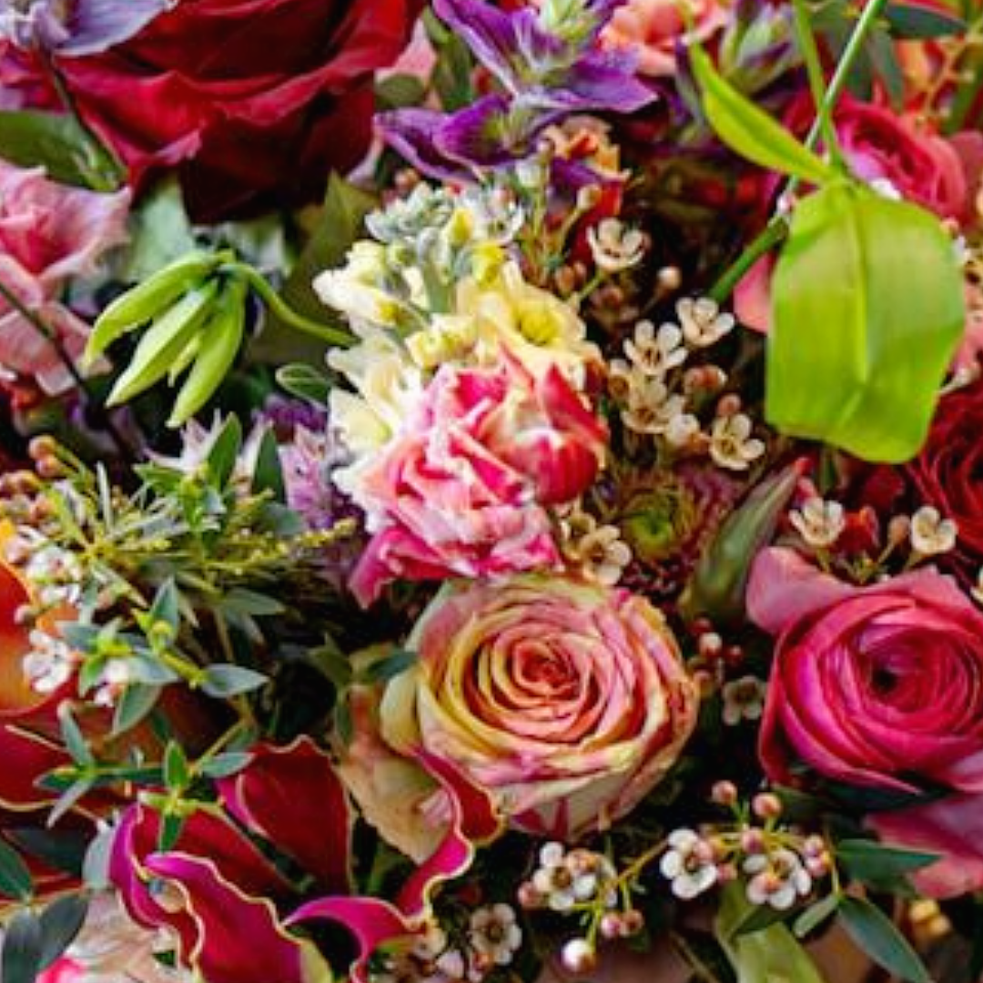Close-up of a vibrant bouquet with roses, carnations, and greenery, in shades of red, pink, and yellow.