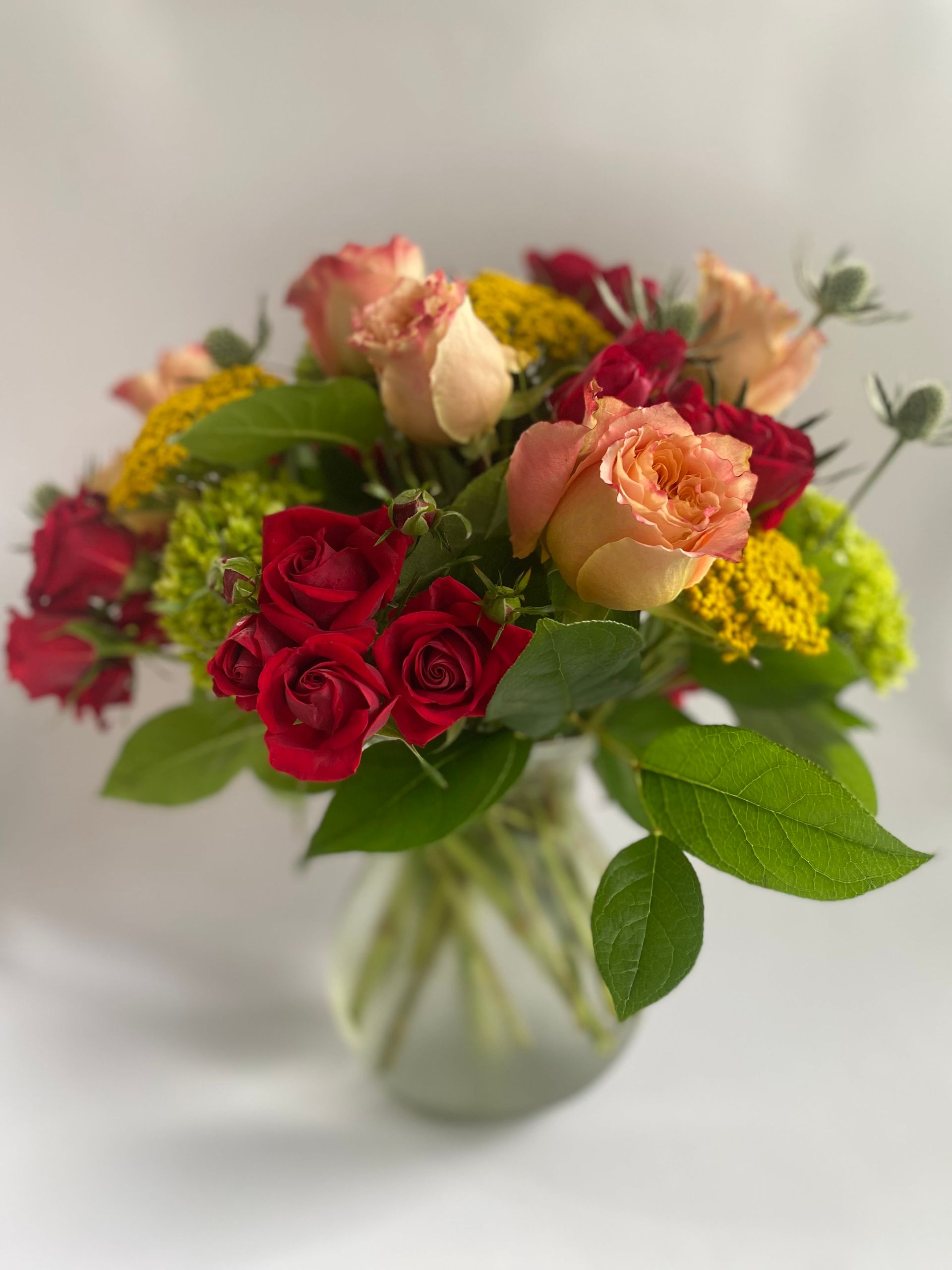 A vase filled with red roses and fall flowers.