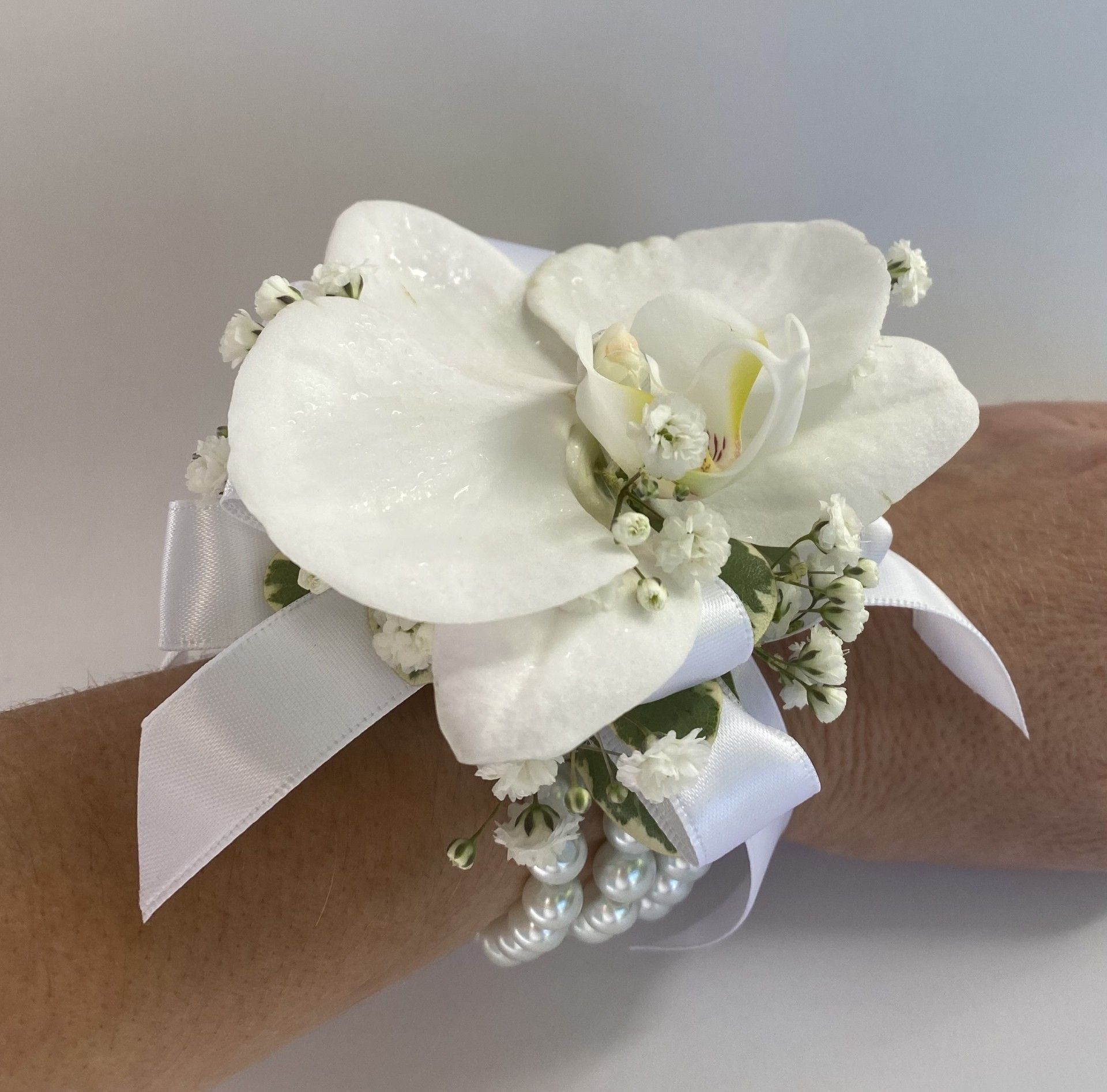 White orchid corsage with baby's breath and ribbon on a wrist.