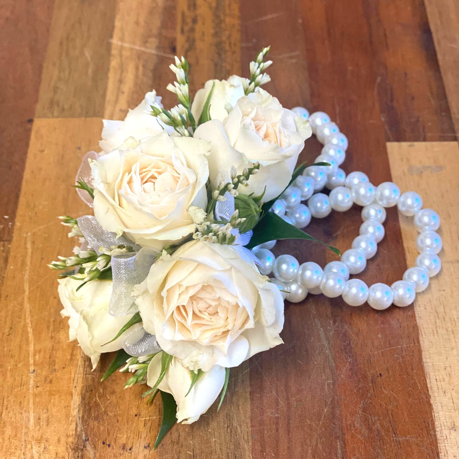 Wrist corsage with pink roses, white ribbons, and baby's breath on a light skin arm.