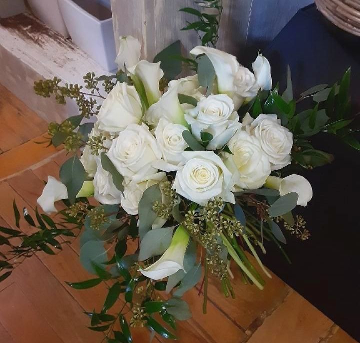 White roses and calla lilies bouquet with greenery on wooden surface.