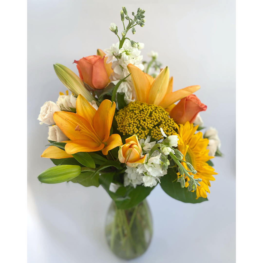 A vase filled with fall flowers including sunflowers and lilies.