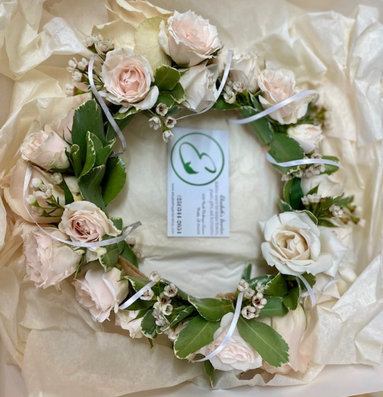 A floral wreath of light pink roses and green leaves on a white background, with a business card in the center.