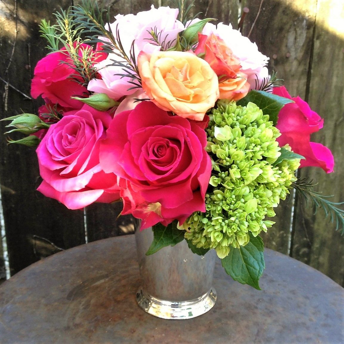 Colorful floral arrangement in a silver vase on a rustic table; roses, hydrangea.