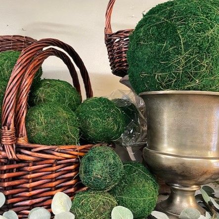 A wicker basket filled with green moss balls is next to a vase filled with green moss balls.