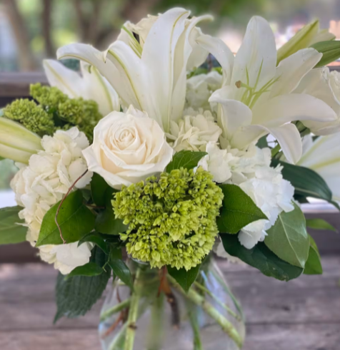 White flower bouquet in a clear vase, including lilies, roses, and hydrangeas.