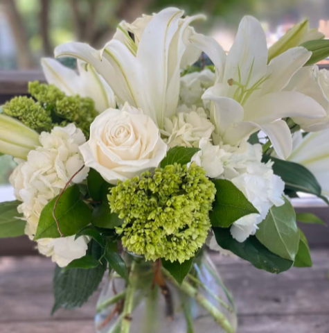 A vase filled with white flowers and green leaves.