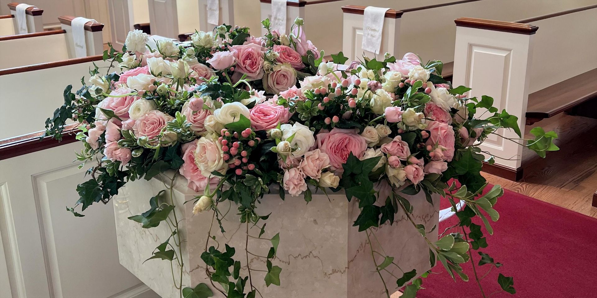 Floral arrangement on a church baptismal font. Pink and white flowers with greenery.