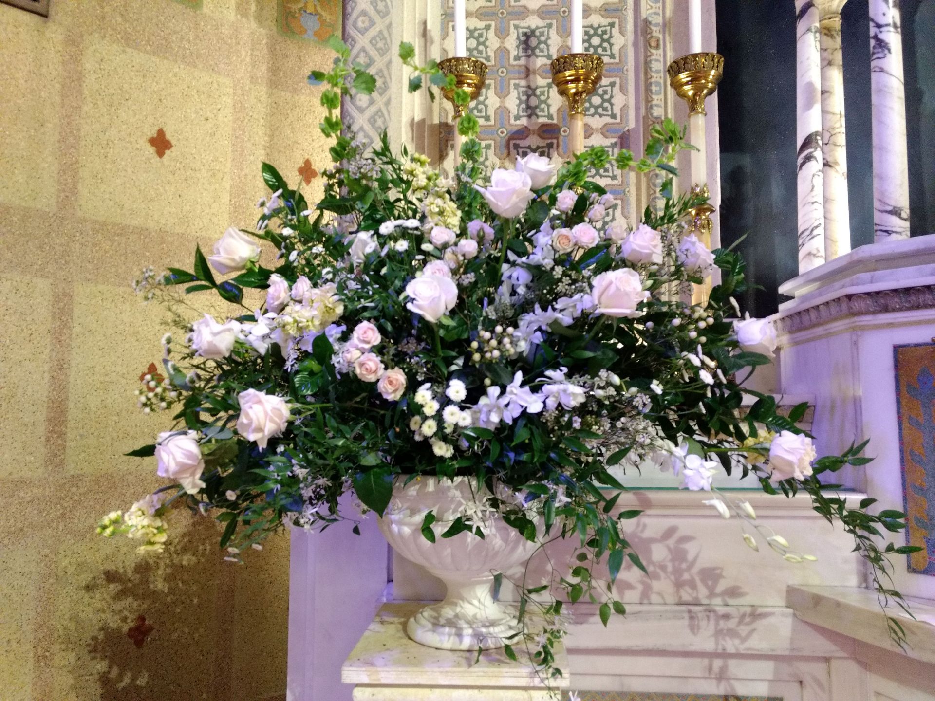 Floral arrangement in an urn on a church altar, featuring white roses and greenery.