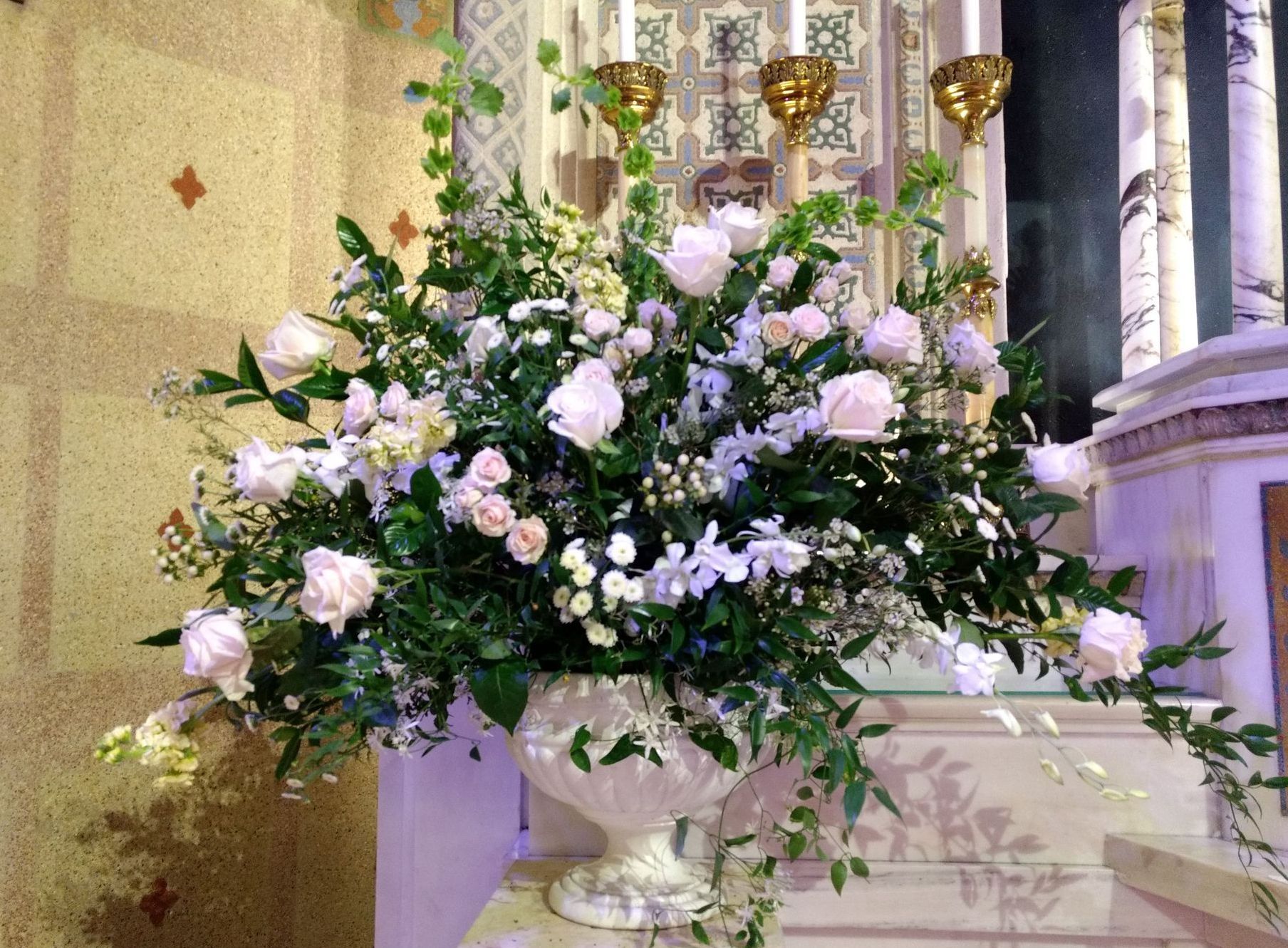 Floral arrangement in a decorative urn, roses, greenery, white and light pink blooms, church interior.