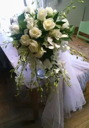 White roses, orchids, and greenery cascade from a floral arrangement on a draped table.