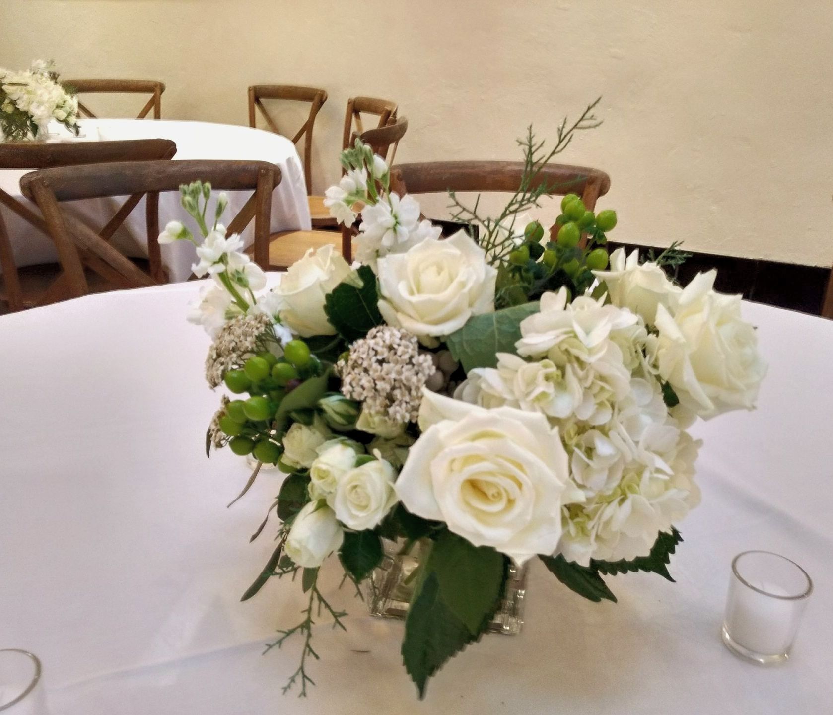 White floral centerpiece on a round table, surrounded by chairs.