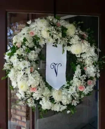 White floral wreath with a banner bearing the letter