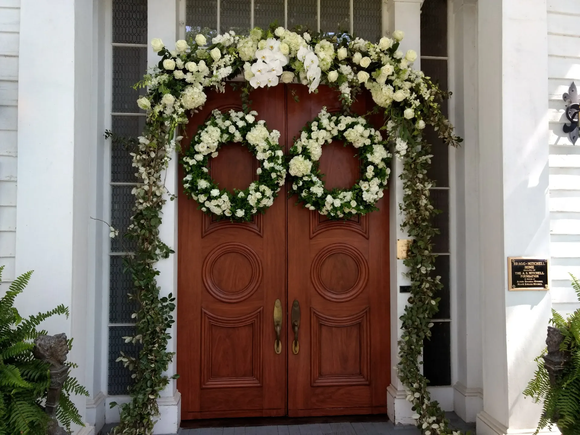 Wooden double doors decorated with white flower wreaths and garlands, exterior view.