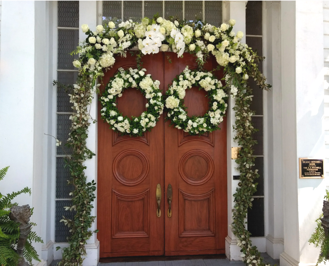 Wooden double doors decorated with white floral wreaths, vines, and a garland.