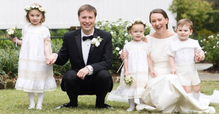 Wedding party poses on grass: Groom, bride, and three children in white outfits.