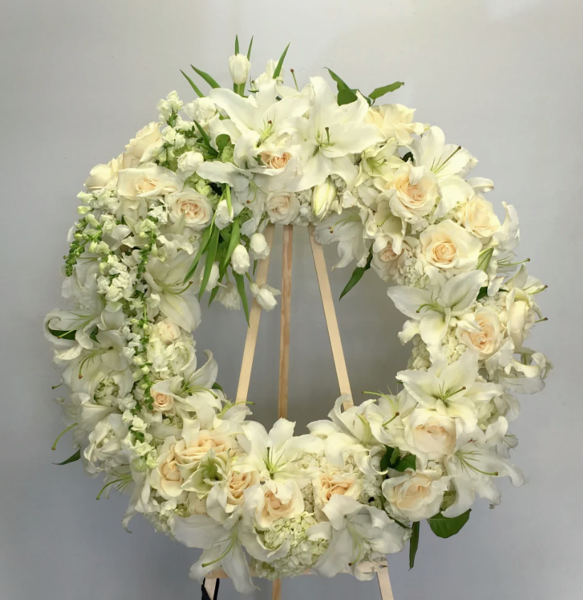 White floral wreath on a wooden stand; used for memorial or funeral, soft whites and greens.