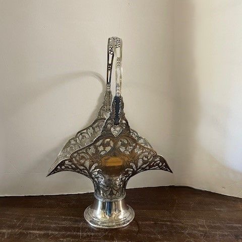 Silver filigree basket with handle on a wooden surface against a white wall.