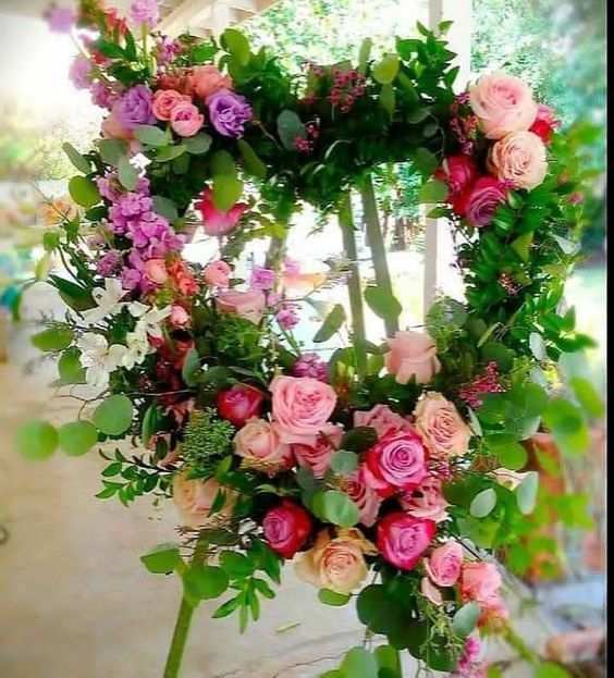 Floral heart-shaped wreath on a stand, featuring pink, red, and purple roses with green foliage.