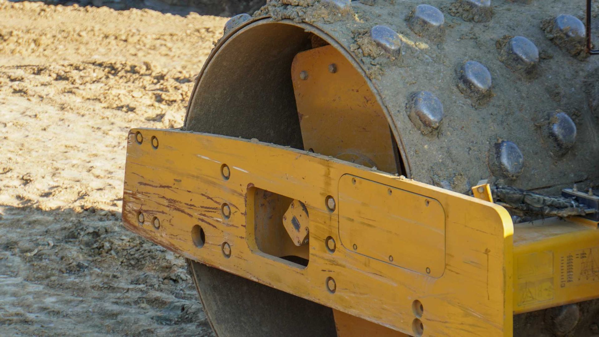 A yellow roller is sitting on top of a dirt field.