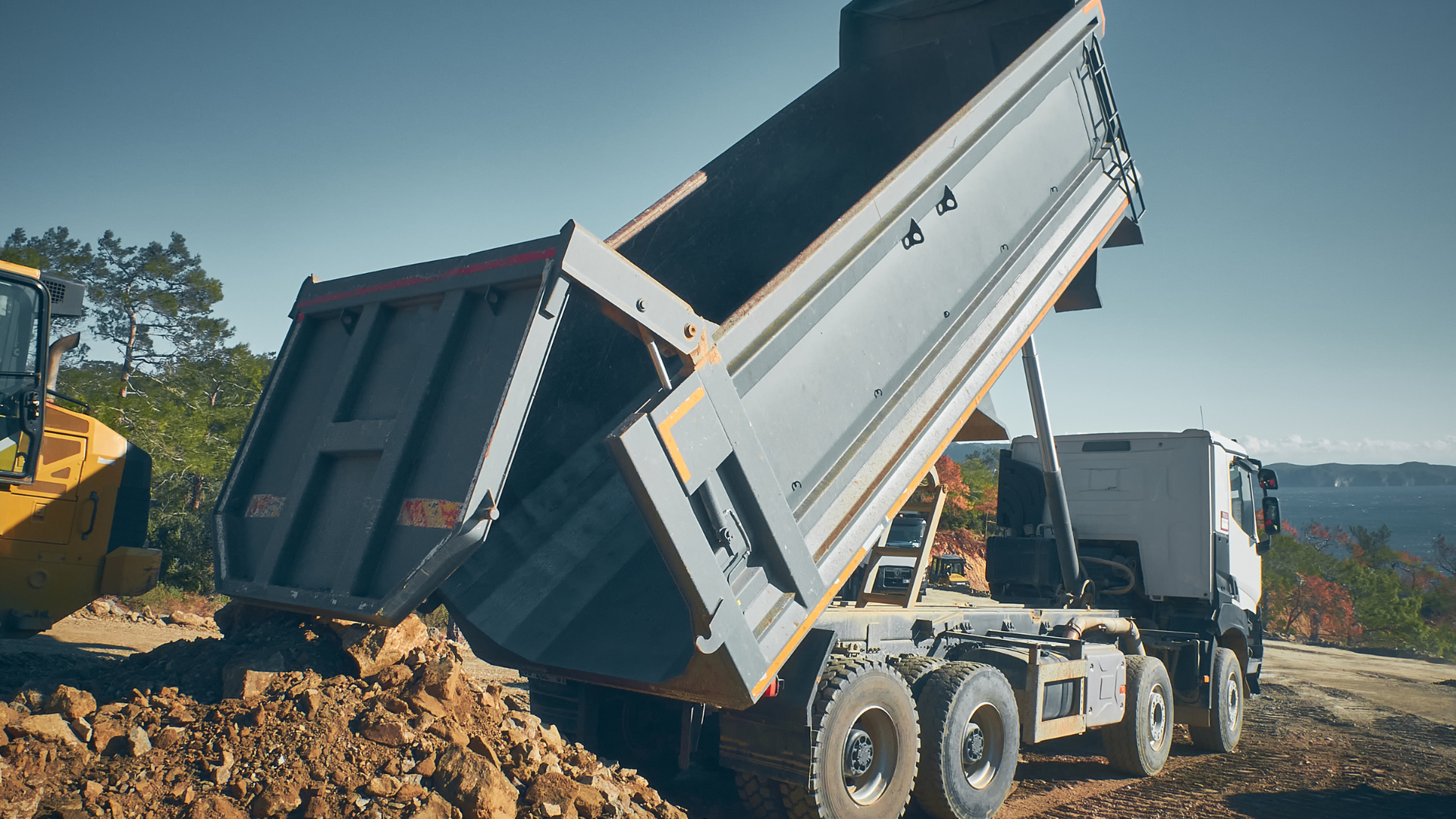 A yellow dump truck is dumping dirt into a pile of dirt.