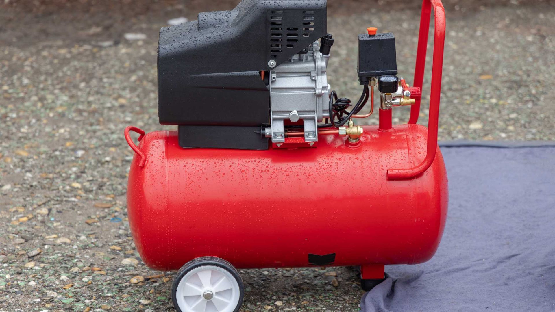 A red air compressor is sitting on a blue towel on the ground.