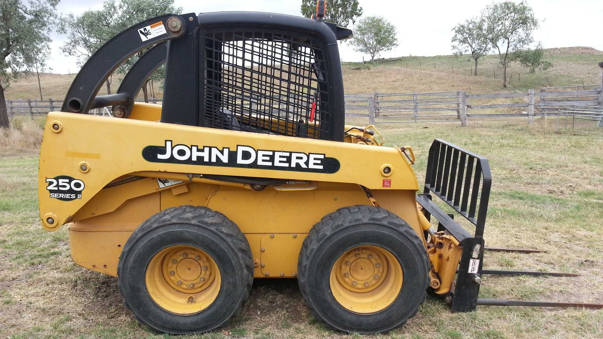 A yellow john deere skid steer is parked in a grassy field