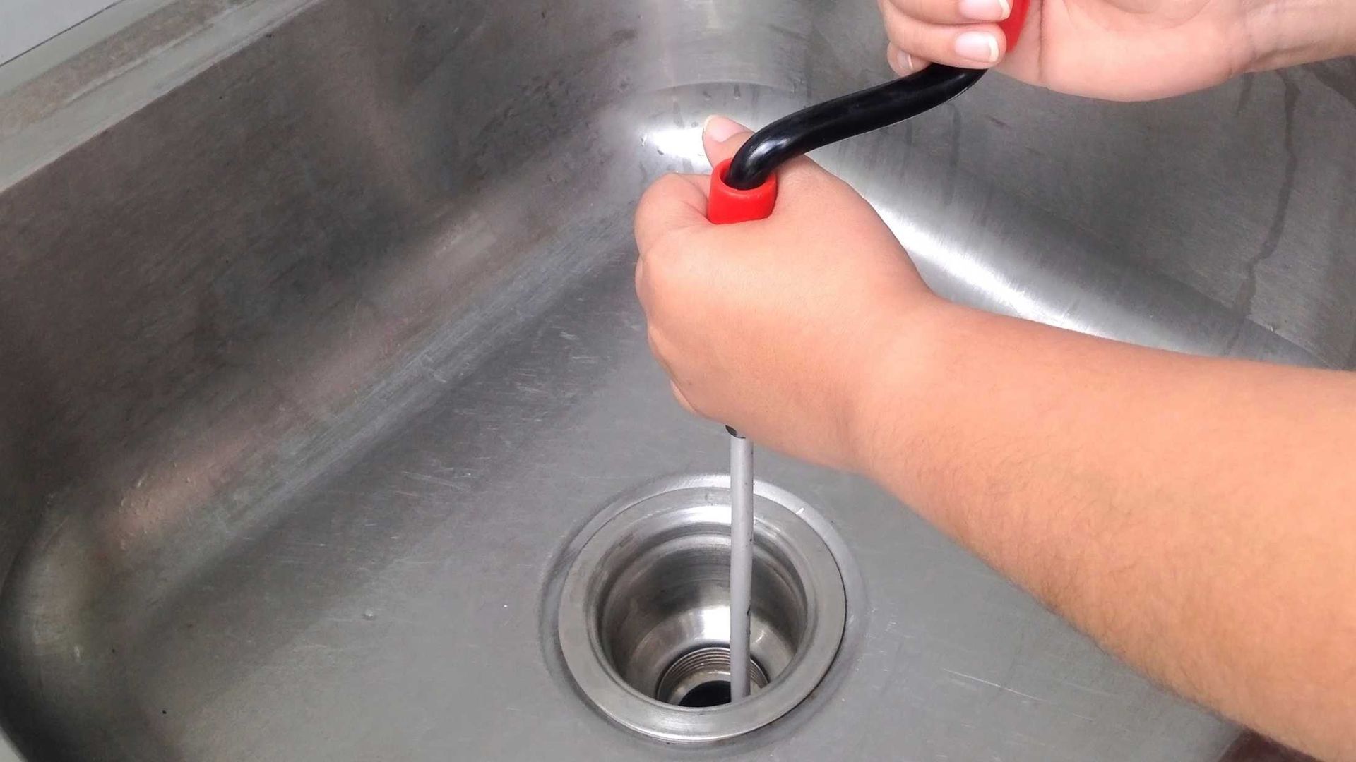 A person is using a plunger to unblock a sink drain.