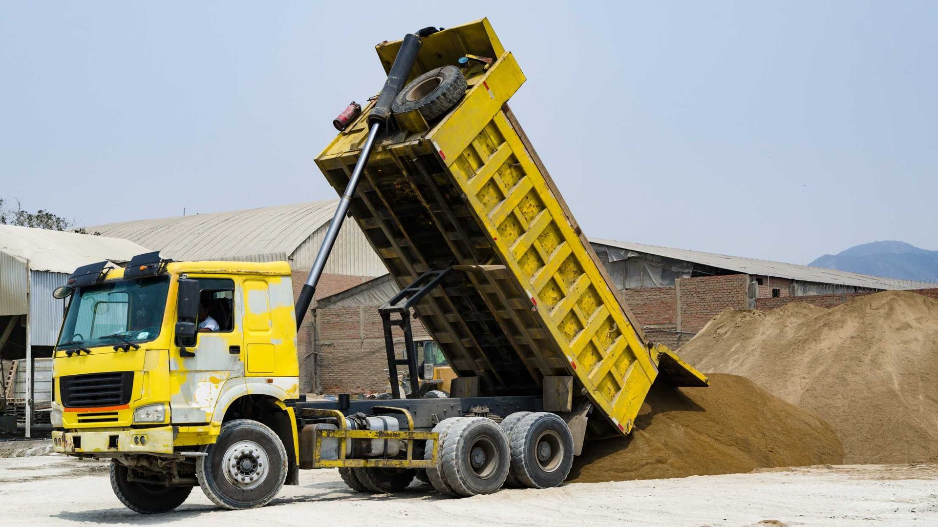 A yellow dump truck is dumping dirt into a pile of dirt.