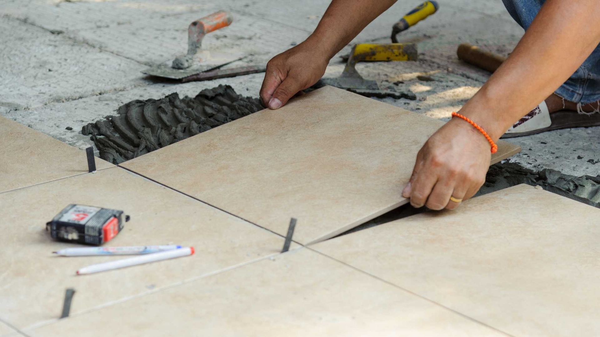 A person is laying tiles on a concrete floor.