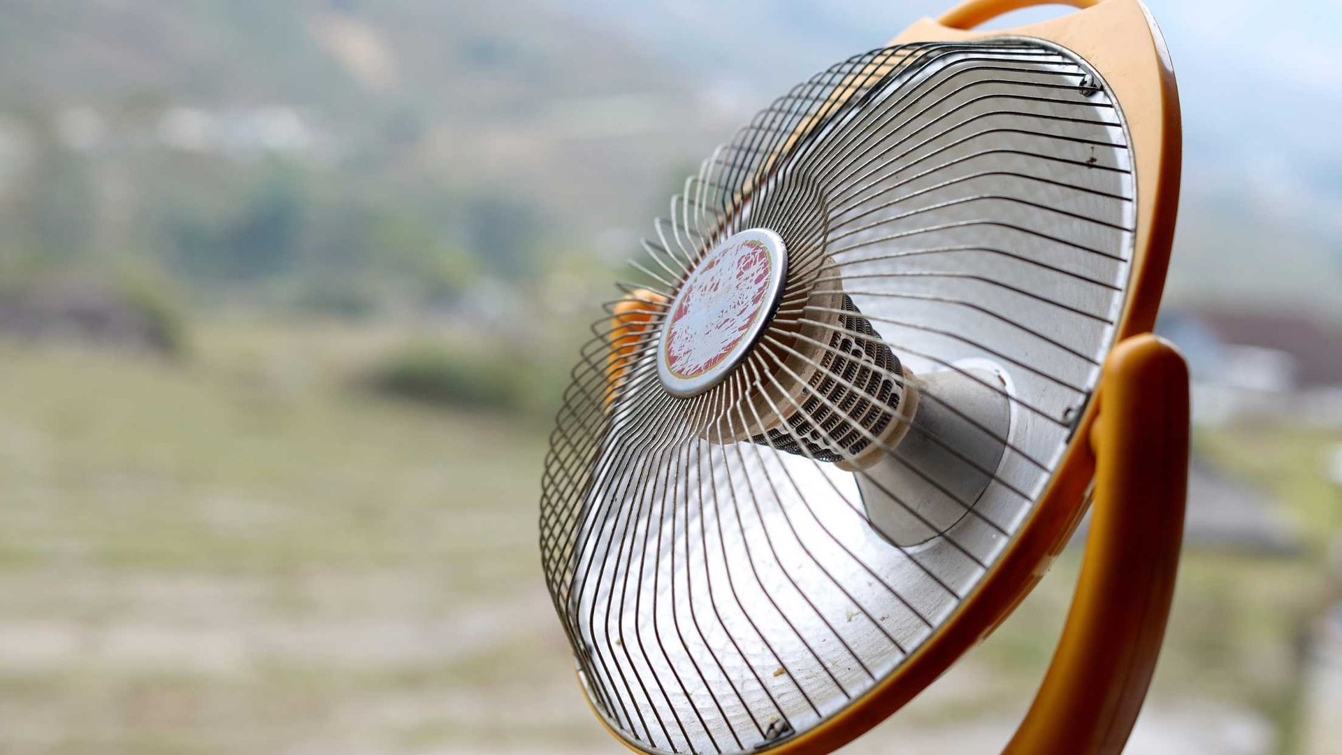 An orange fan is sitting in front of a window.