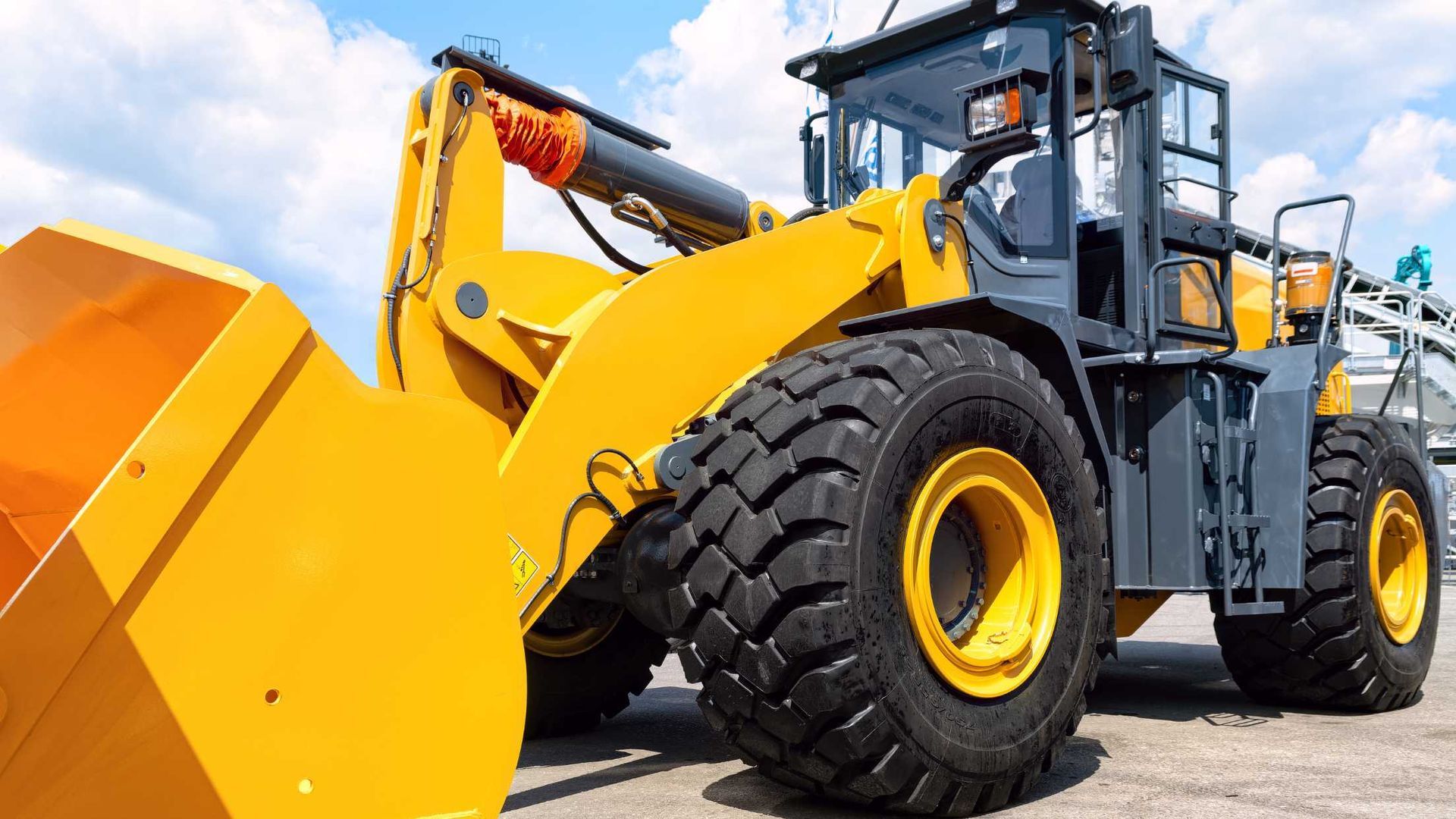 A yellow bulldozer with a large orange bucket is parked on the side of the road.
