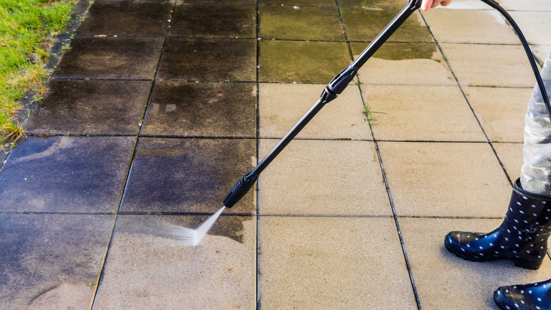 A person is using a high pressure washer to clean a sidewalk.