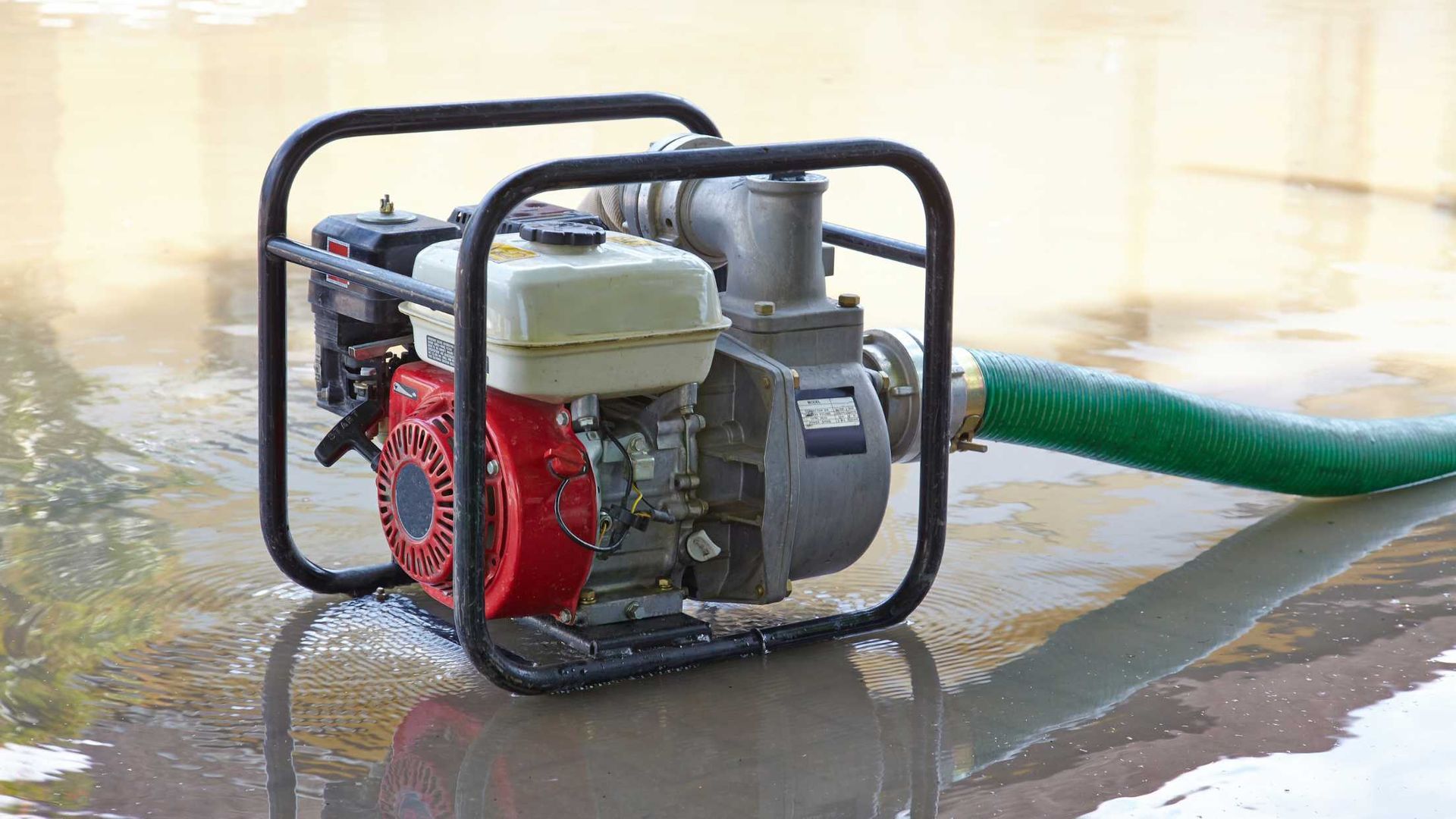 A water pump with a green hose attached to it is sitting in a puddle of water.
