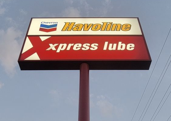 Sign for Havoline Xpress Lube, red and white on a brown pole against a cloudy sky.