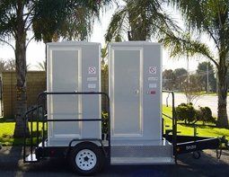Two portable toilets on a trailer are parked next to each other.