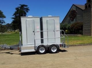 A trailer with two toilets attached to it is parked in a parking lot.
