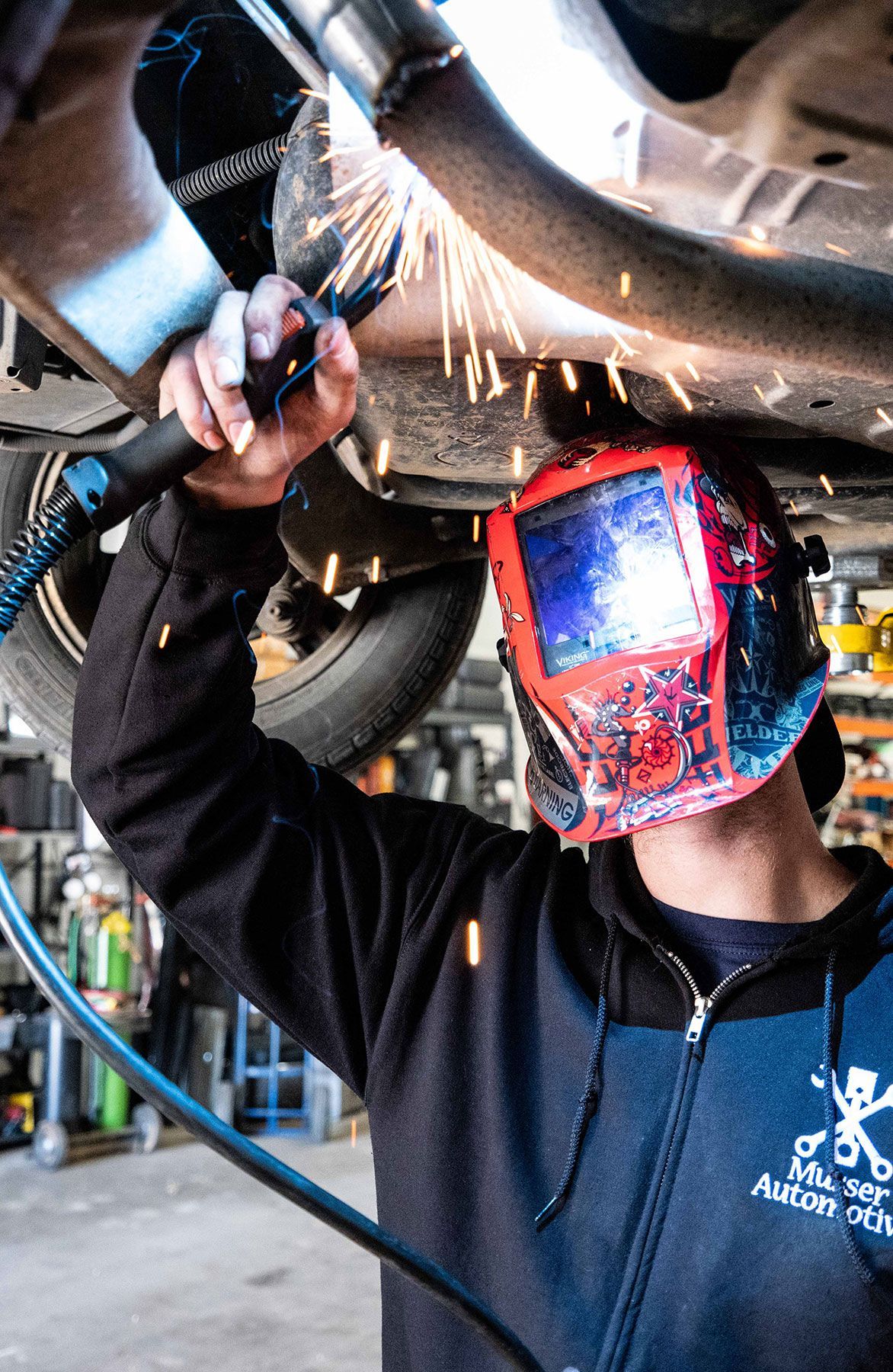 Technician welding a vehicle’s exhaust on a lift while wearing a welding mask at Musser Automotive.