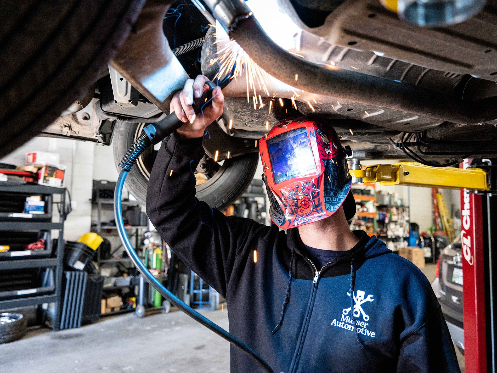 A certified technician wearing a welding mask repairing a car exhaust pipe at Musser Automotive in bowling green kentucky