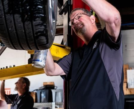 Service manager Dwayne checking a tire for leaks on a lift, with senior technician assisting at Musser Automotive.