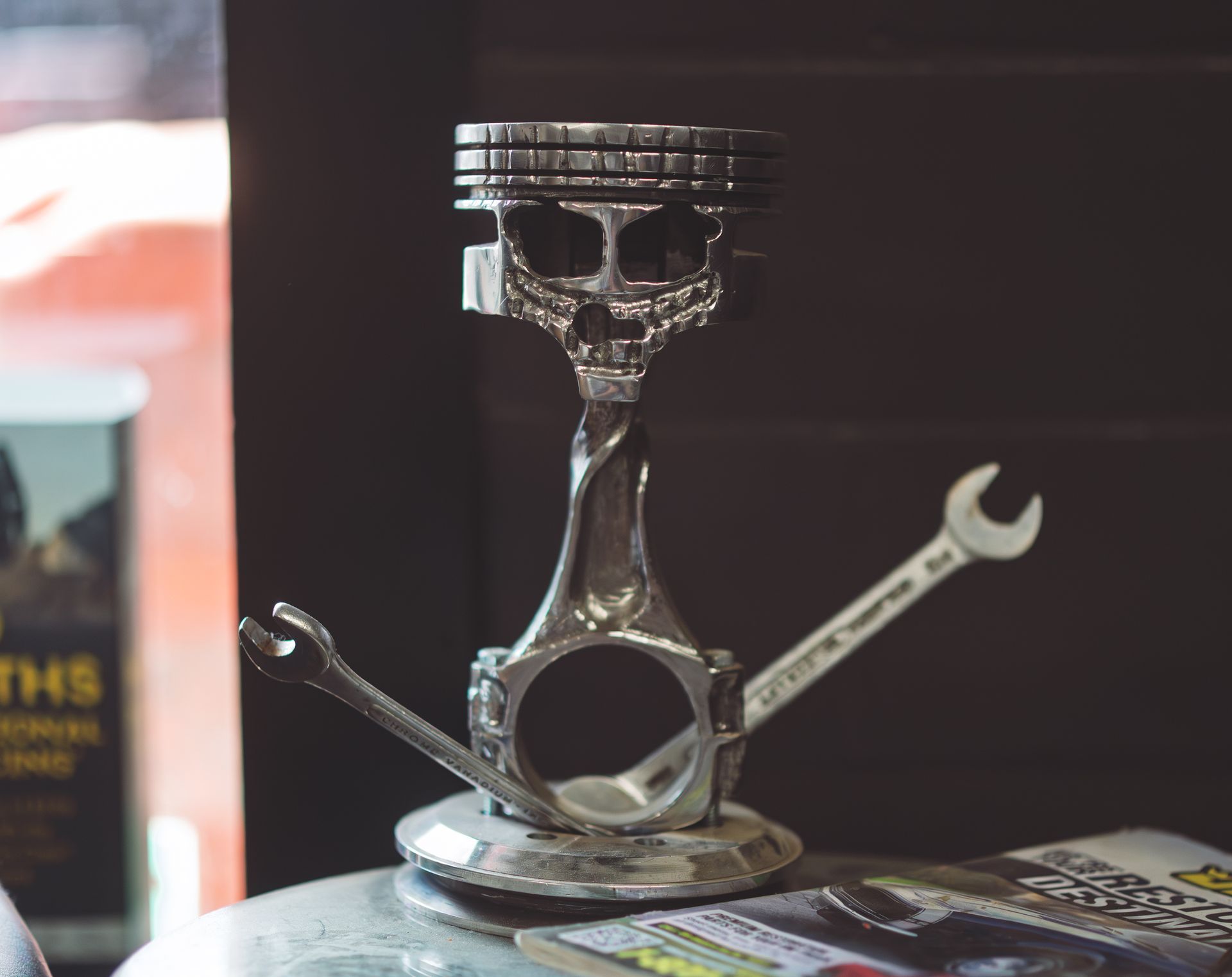 Sculpture of a skull made from engine parts, with wrenches as arms, on a metal base. | Musser Automotive
