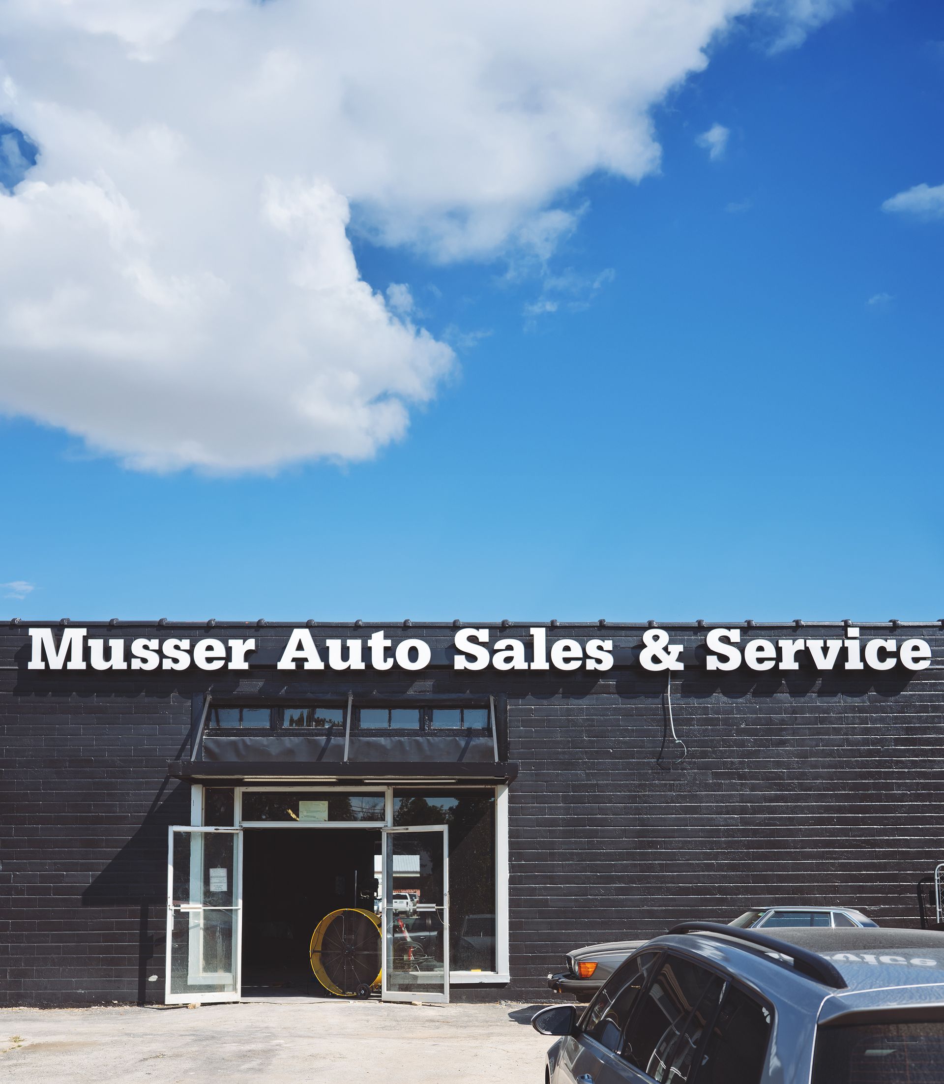 Musser Auto Sales & Service building with dark exterior under a blue sky with clouds. Cars are parked in front. | Musser Automotive
