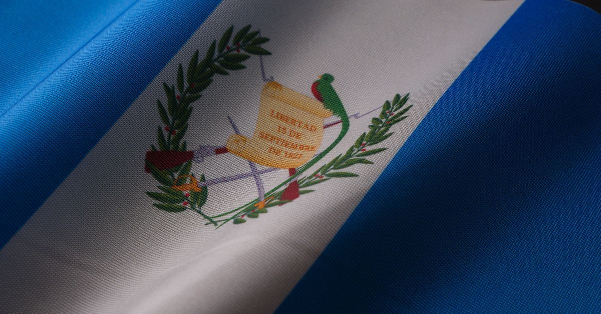Bandera de Guatemala ondeando, azul y blanca con el escudo nacional en el centro.