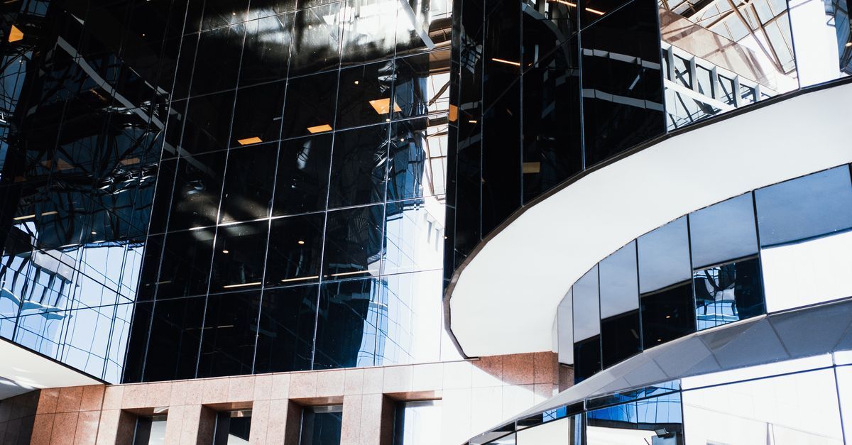 Edificio moderno de cristal con fachada blanca curvada y ventanas reflectantes bajo la luz del día brillante.
