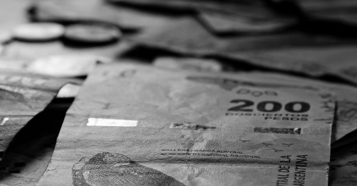 Primer plano de un billete de 200 sobre una mesa con monedas borrosas al fondo.