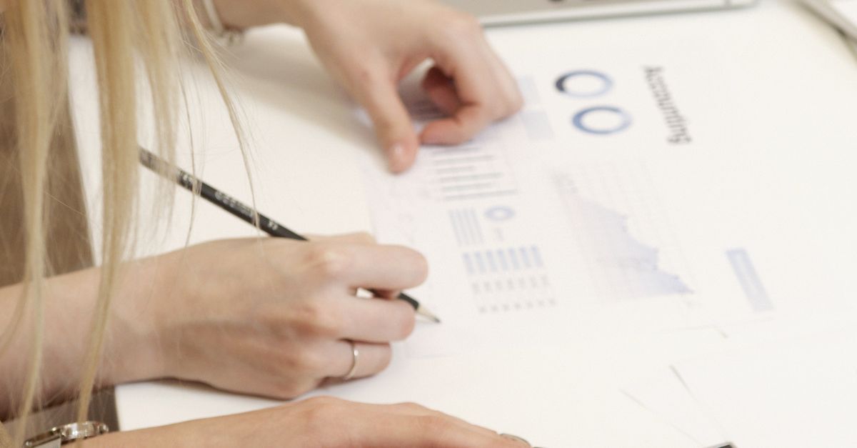 Manos con un bolígrafo revisando gráficos y tablas impresos sobre un escritorio blanco.