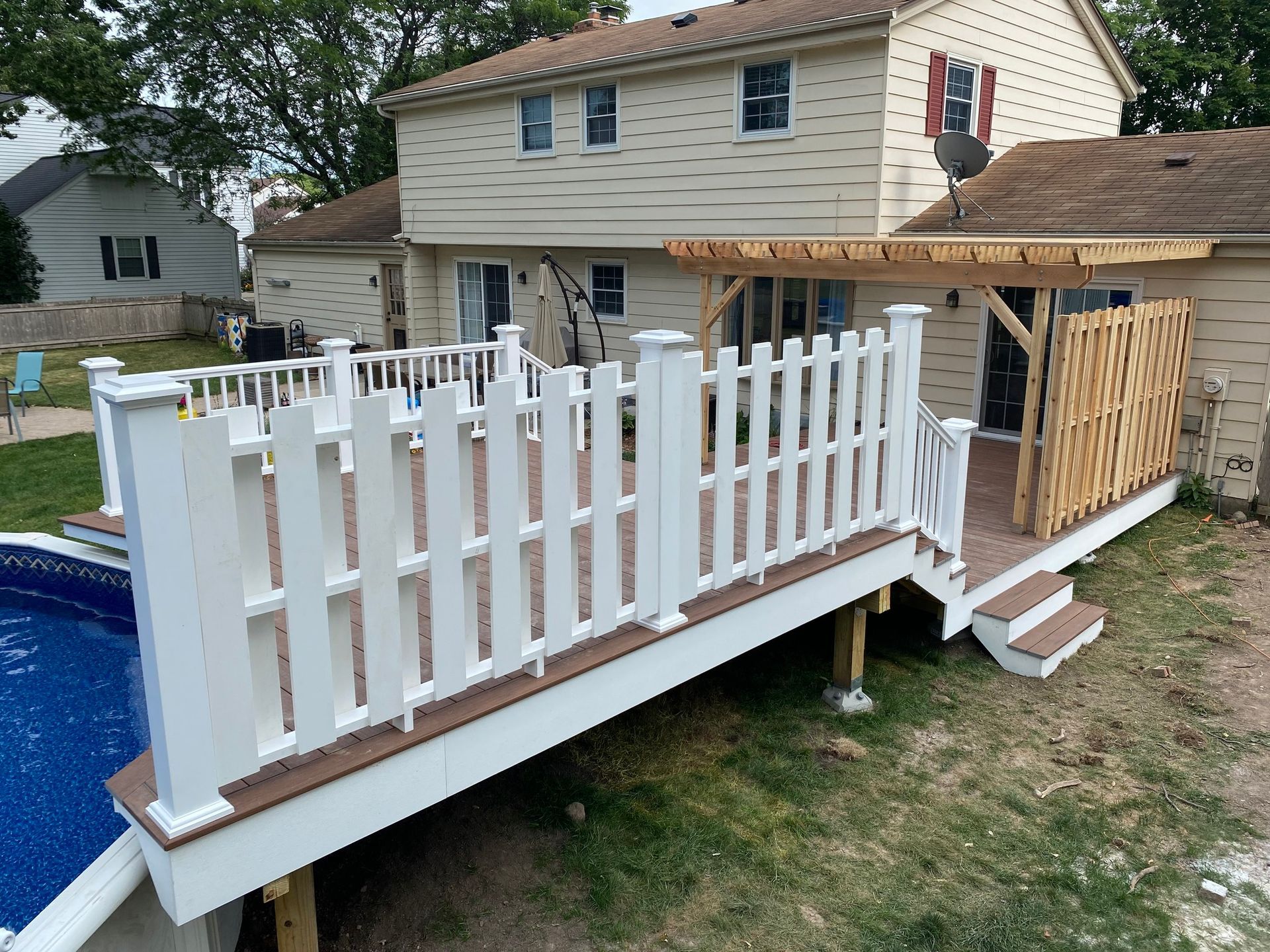 White deck with picket fence surrounds a pool; house in background.