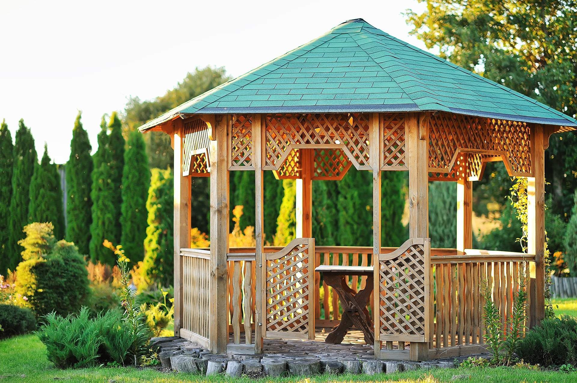 Wooden gazebo with teal roof in a lush garden, surrounded by trees and greenery